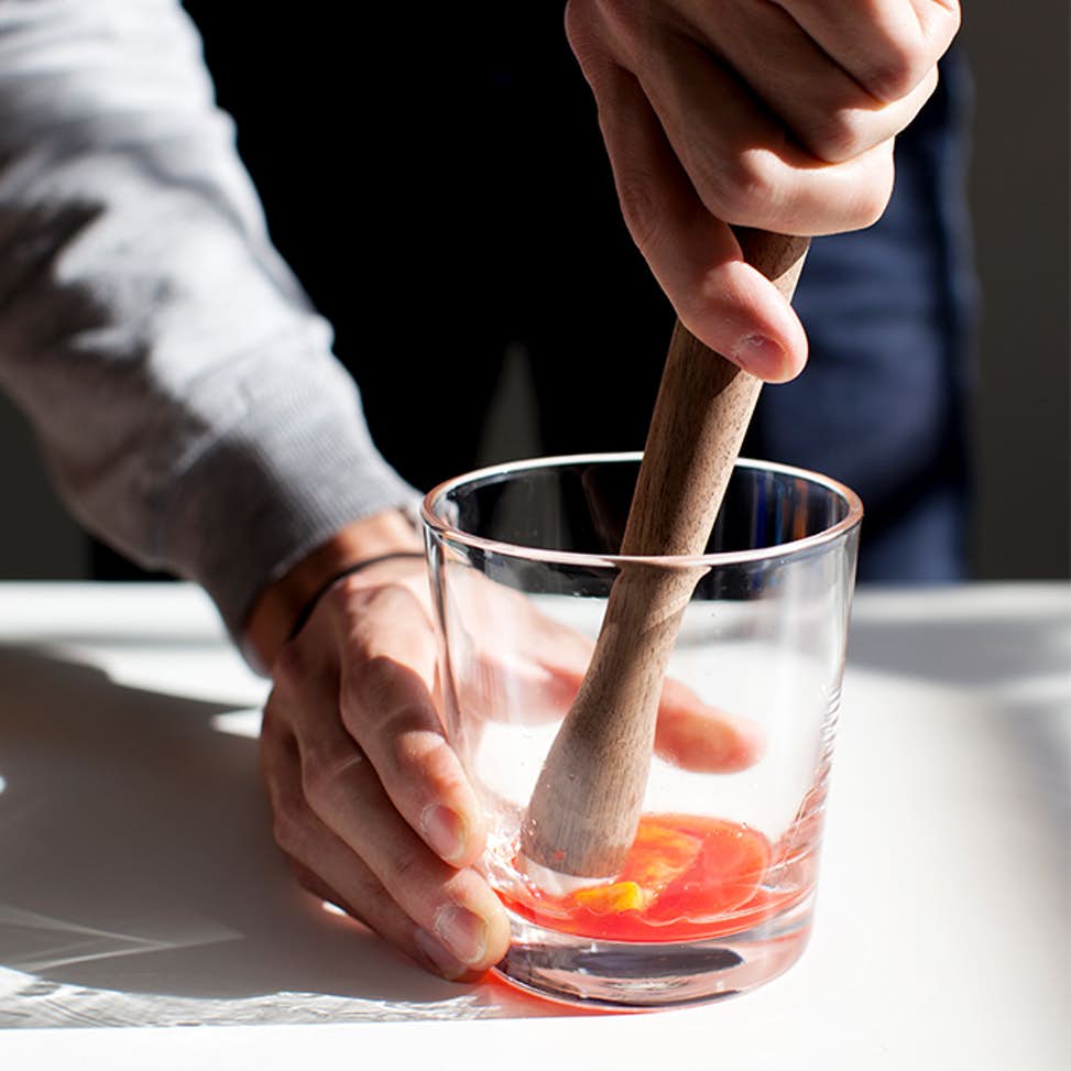 A bartender uses a muddler bartending tool to grind up cocktail ingredients