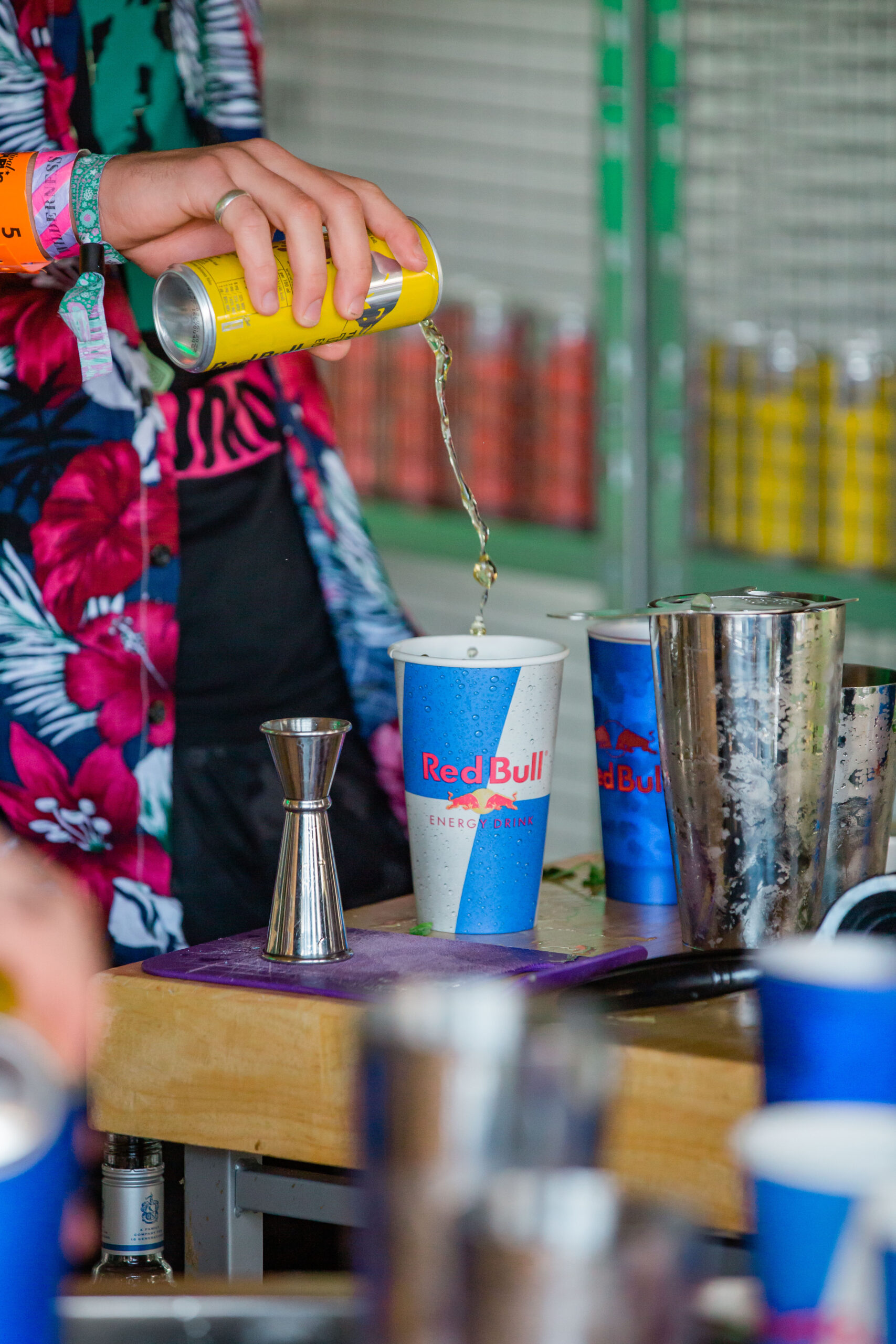 A man in a flower patterned shirt pours a Red Bull ready to drink cocktail into a blue Red Bull branded cup at the Red Bull Lab at Wilderness Festival