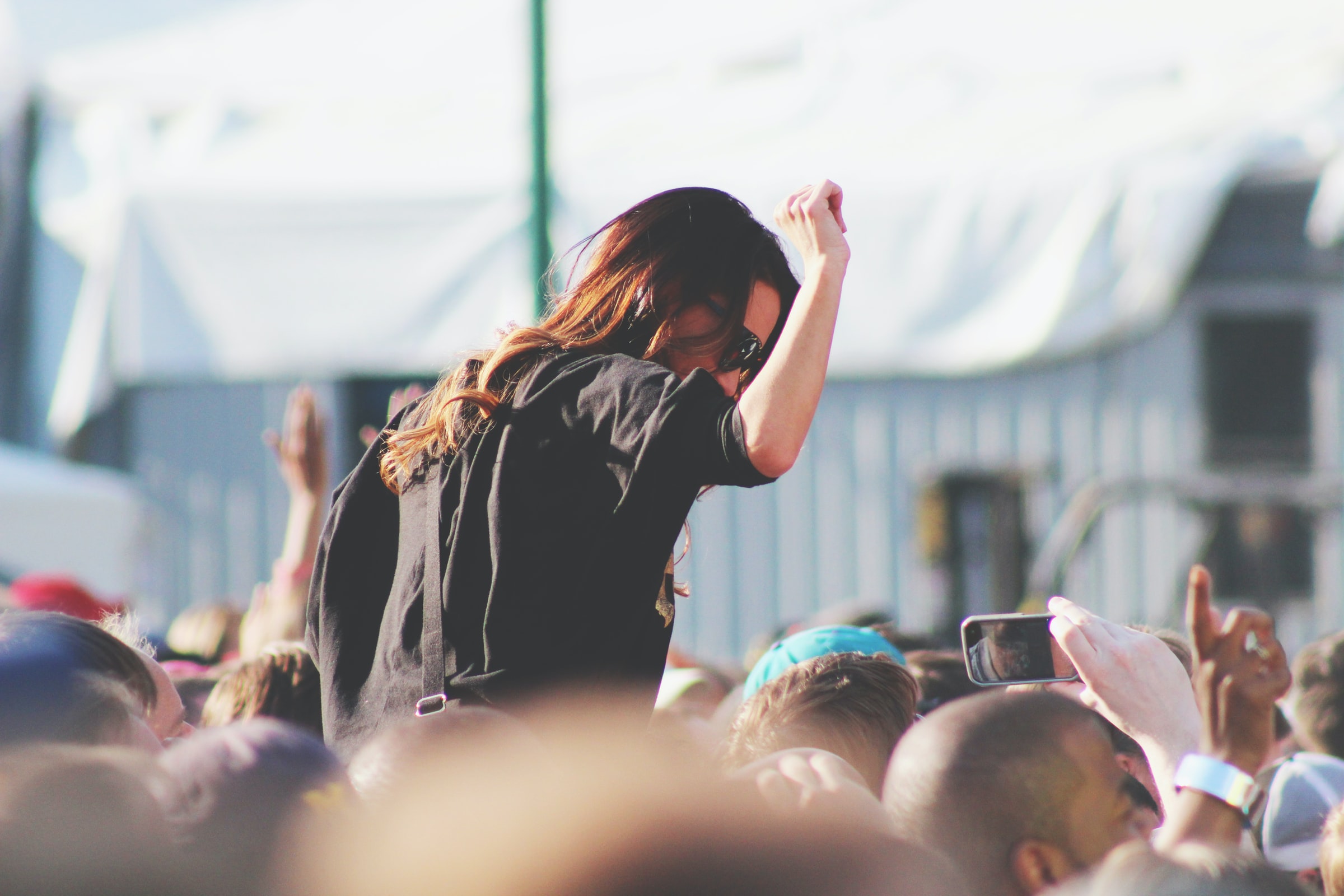 A woman with sunglasses dances on the shoulders at a festival, above the crowd.