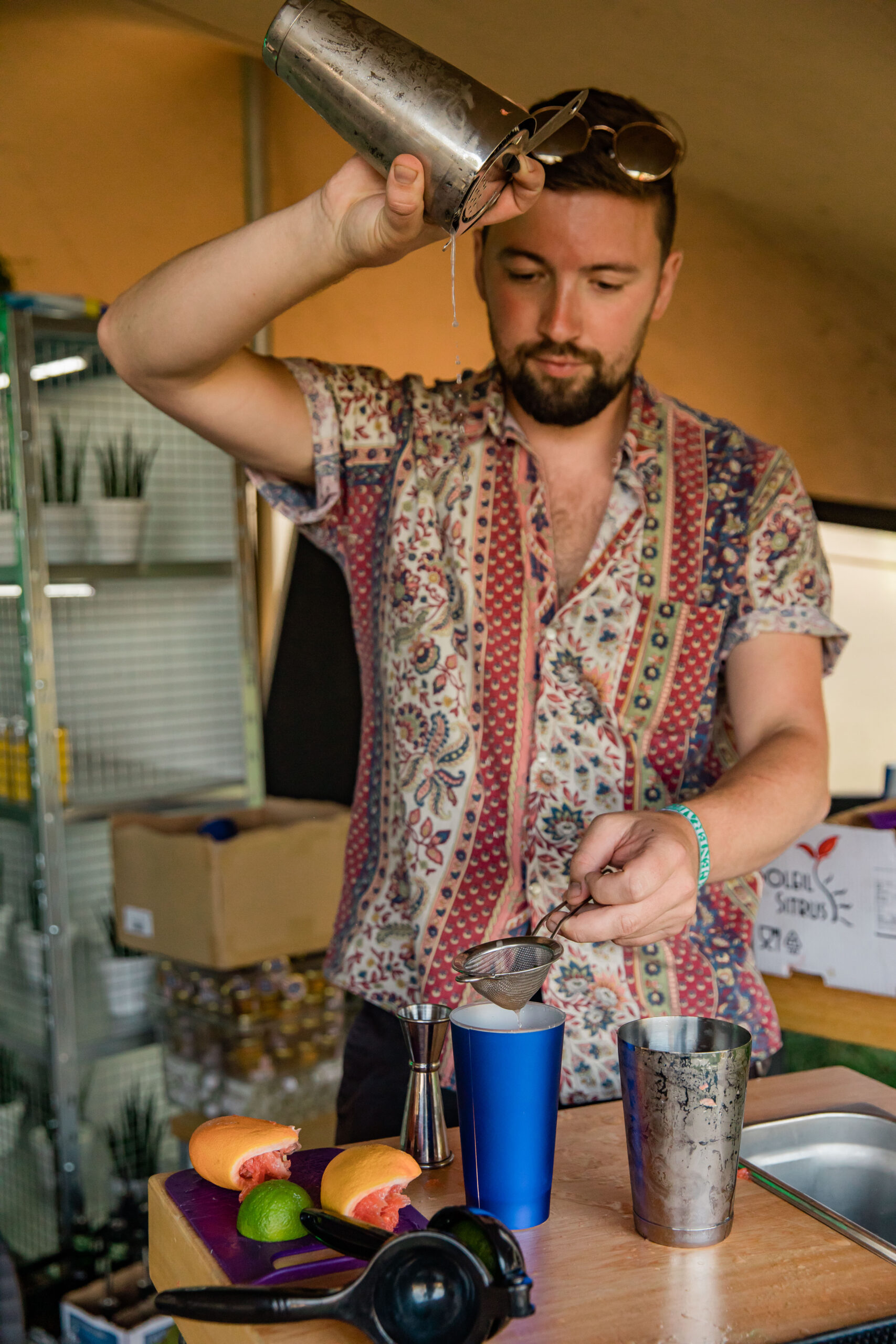 A man in a flower patterned shirt pours a cocktail from a shaker into a blue Red Bull shaker tin at the Red Bull Lab at Wilderness Festival