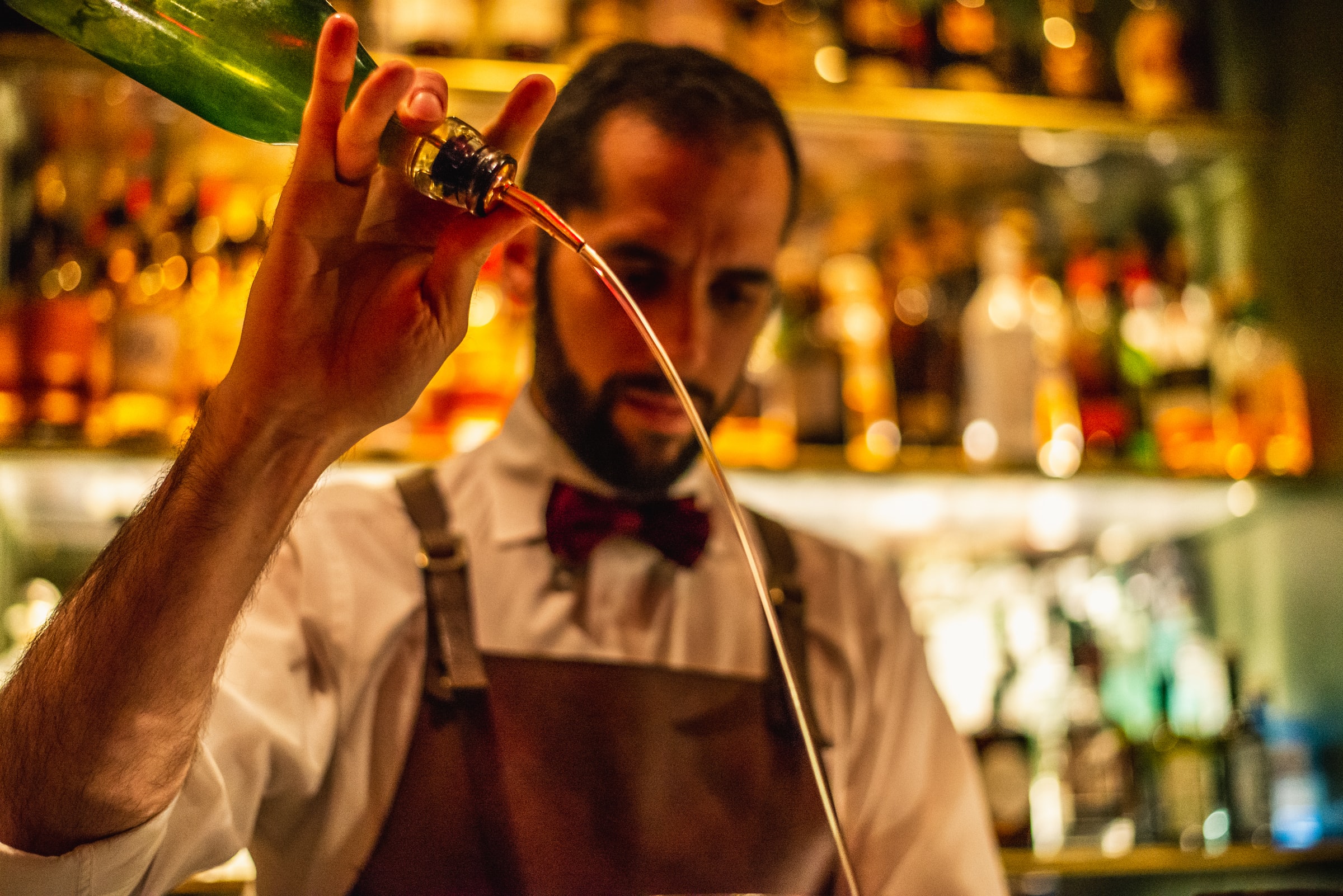 A bartender in bow tie pours a spirit 