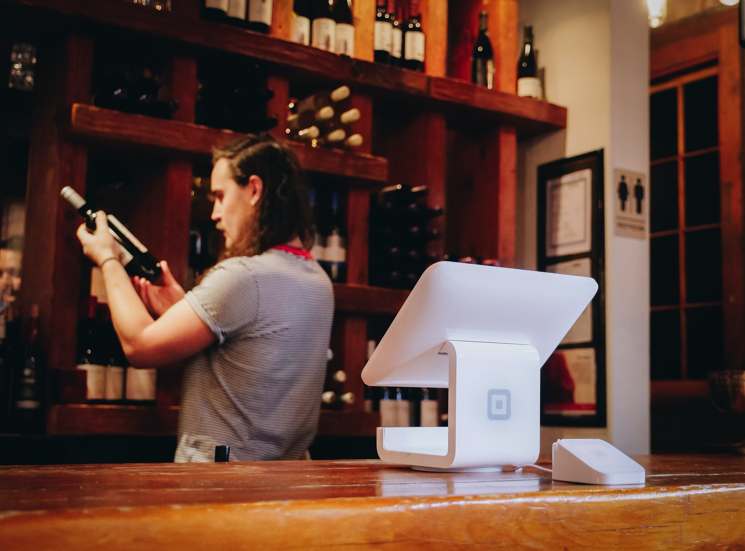 A bar back puts wine onto a shelf, show important it is to keep the bar stocked, a key factor when hiring a bartender