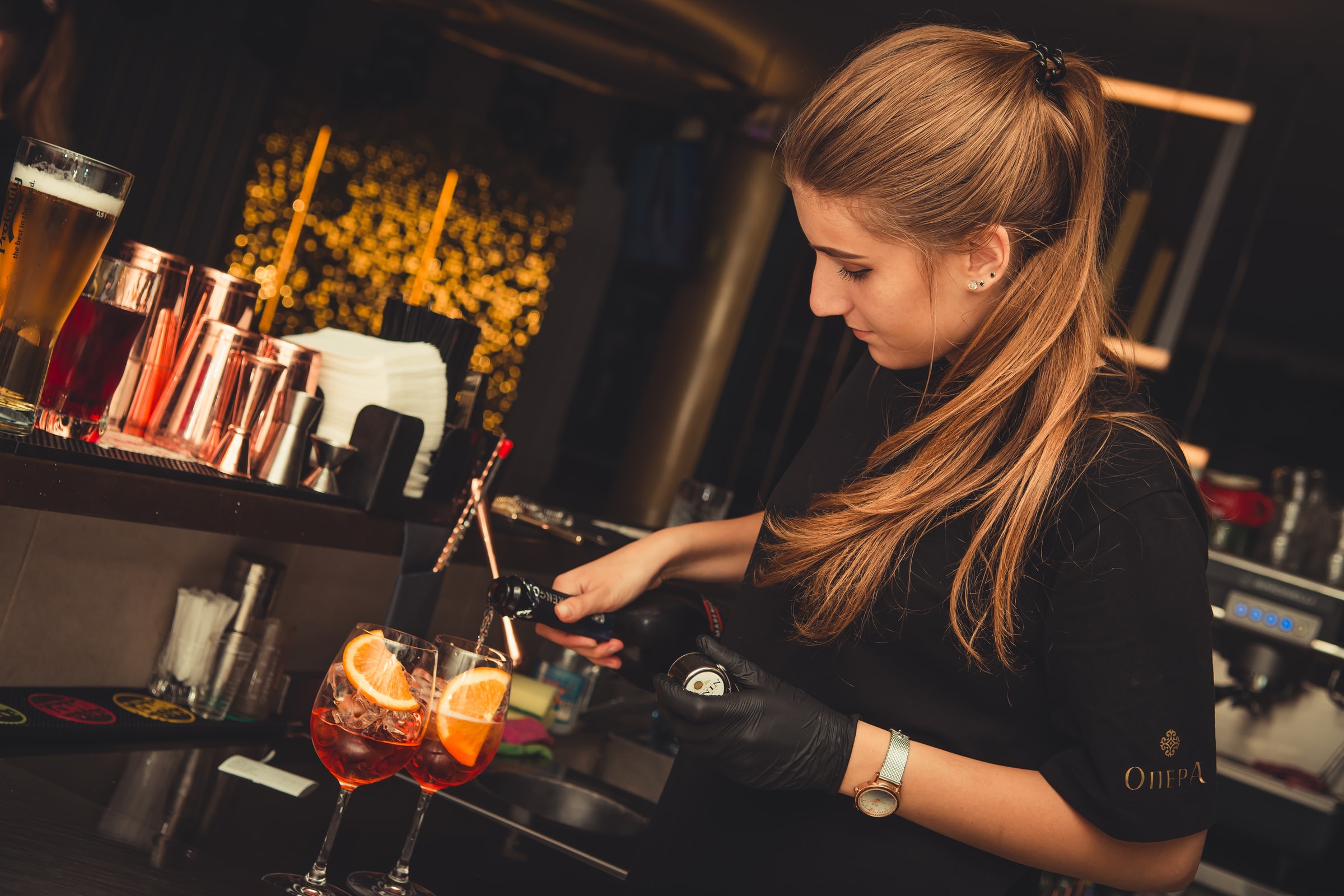 A female bartender multitasks by pouring drinks whilst looking at an order slip
