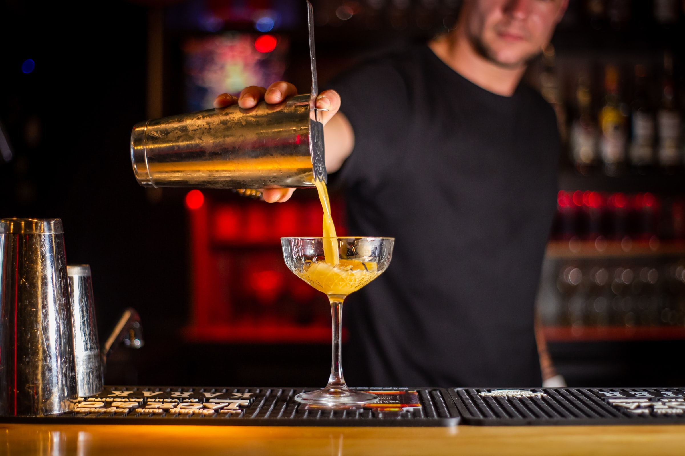 A bartender pours a cocktail from a cocktail shaker into a coupe glass