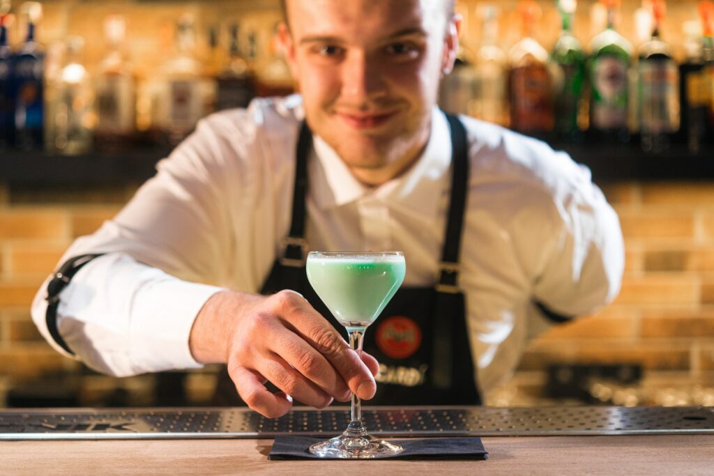 A bartender presents a green cocktail to the camera