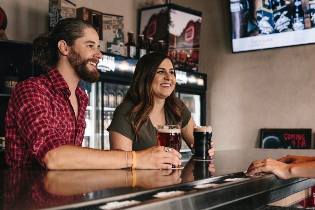 Two guests at the bar smile as they listen to a bartender speak about drinks