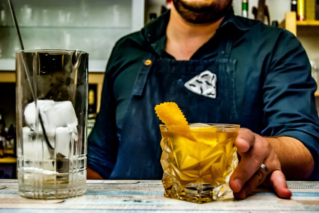 A bartender passes a cocktail in a rocks glass over the bar